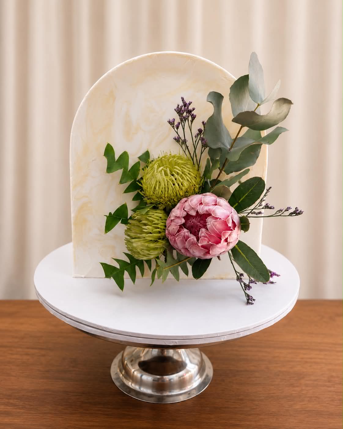 Single tier yellow buttercream cake with a twisted rope heart outline on the side and rope border around the base on a silver cake stand